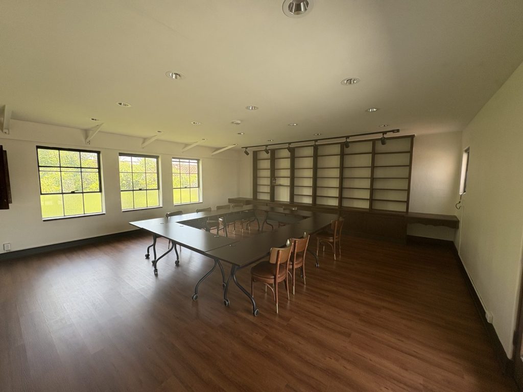 The library set up for a seminar, with tables arranged in a square beneath a row of windows.