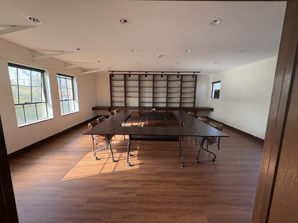 Seminar tables arranged in a square in the sunlit library, with built-in shelves along the far wall.